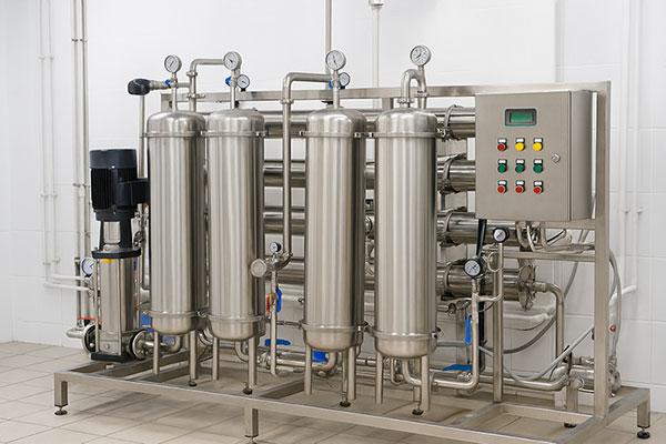 Industrial stainless steel reverse osmosis (RO) system with pressure vessels and control panel in a food manufacturing facility.